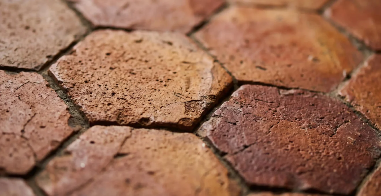 Gros plan sur des tomettes anciennes en terre cuite disposées sur un sol, révélant leur patine authentique et leurs nuances naturelles de rouge, ocre et brun
