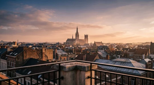 Vue en contre-jour depuis une terrasse d'appartement donnant sur les toits d'une ville historique et la silhouette d'un monument emblématique au loin